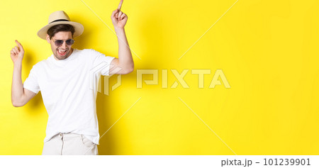 Tourism, travelling and holidays concept. Male tourist enjoying vacation, dancing in straw hat and sunglasses, pointing fingers sideways 101239901