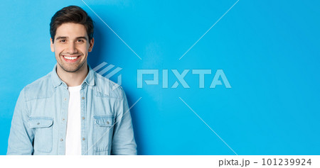 Close-up of young successful man smiling at camera, standing in casual outfit against blue background Close-up of young successful man smiling at camera, standing in casual outfit against blue background 101239924