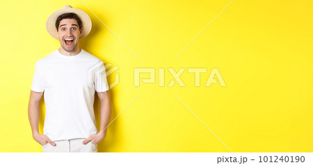 Surprised man tourist in straw hat looking happy, react amazed to travel agency advertisement, standing over yellow background 101240190