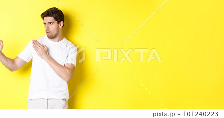 Man showing kung-fu skills, martial arts ninja movement, standing in white t-shirt ready to fight, standing over yellow background 101240223