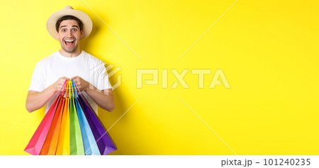 Image of happy man shopping on vacation, holding paper bags and smiling, standing against yellow background Image of happy man shopping on vacation, holding paper bags and smiling, standing against yellow background 101240235