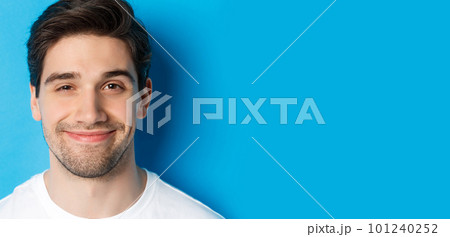 Headshot of attractive man smiling pleased, looking intrigued, standing over blue background Headshot of attractive man smiling pleased, looking intrigued, standing over blue background 101240252