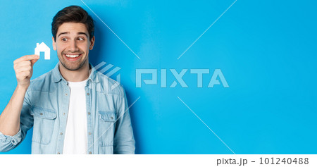 Real estate concept. Excited guy looking at small house model and smiling, renting apartment, standing over blue background 101240488