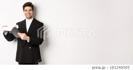 Image of confident businessman in suit looking at documents, holding clipboard and smiling pleased, standing against white background 101240505