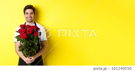 Smiling florist in black apron holding flowers, selling bouquet of roses, standing over yellow background 101240550