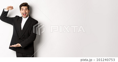 Portrait of excited handsome man in suit, shaping big object on copy space and smiling amazed, holding something, standing over white background Portrait of excited handsome man in suit, shaping big object on copy space and smiling amazed, holding something, standing over white background 101240753