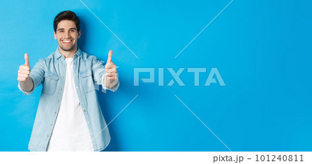 Smiling confident man showing thumbs up, guarantee quality, approving something good, standing against blue background 101240811