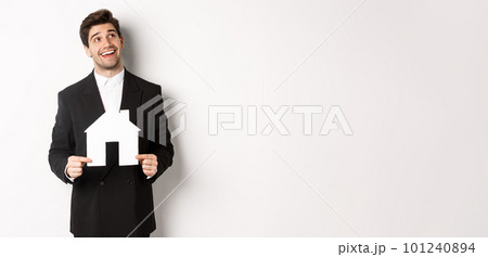 Portrait of handsome man in suit searching for home, holding paper house and looking at upper right corner dreamy, standing over white background Portrait of handsome man in suit searching for home, holding paper house and looking at upper right corner dreamy, standing over white background 101240894