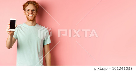 Handsome redhead man in glasses showing blank smartphone screen and smiling, demonstrate online promo or application, standing over pink background Handsome redhead man in glasses showing blank smartphone screen and smiling, demonstrate online promo or application, standing over pink background 101241033