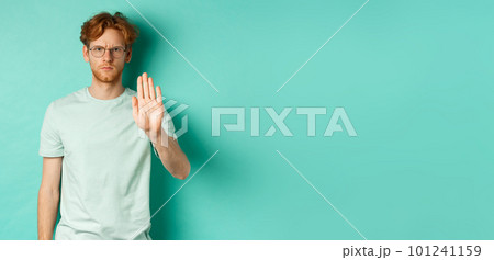 Angry and serious young man with red hair, wearing glasses, showing stop gesture, telling no, disapprove and prohibit something bad, standing over turquoise background Angry and serious young man with red hair, wearing glasses, showing stop gesture, telling no, disapprove and prohibit something bad, standing over turquoise background 101241159