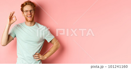 Cheerful guy with red hair and beard, wearing glasses, showing OK sign in approval and saying yes, smiling satisfied, standing over pink background 101241160