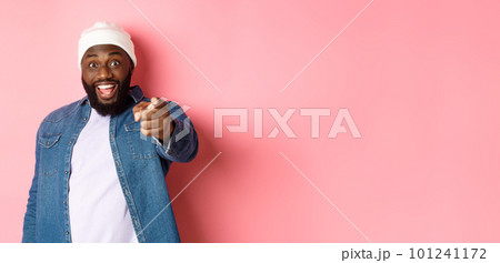 Happy african-american hipster man pointing finger at camera, need you, smiling excited, standing over pink background Happy african-american hipster man pointing finger at camera, need you, smiling excited, standing over pink background 101241172