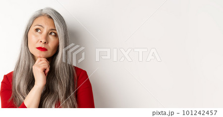 Close up of thoughtful asian business woman looking at upper left corner, thinking or making choice, standing over white background Close up of thoughtful asian business woman looking at upper left corner, thinking or making choice, standing over white background 101242457