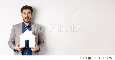 Real estate. Excited business man in suit holding paper house cutout and looking amazed at camera, buying apartment, white background 101242470