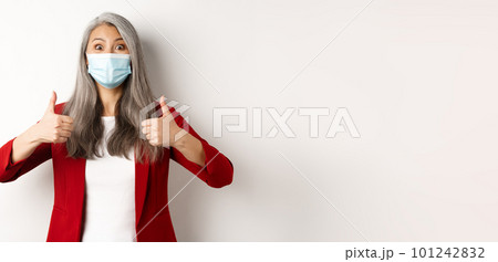 Coronavirus and business concept. Asian female manager in face mask looking cheerful, showing thumb-up in approval, white background 101242832