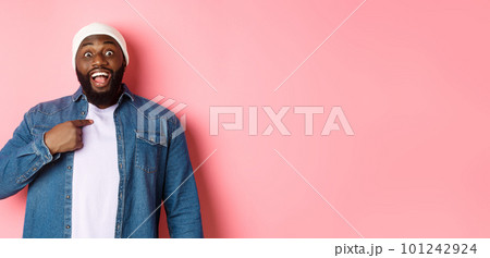 Surprised Black man in hipster beanie pointing at himself, staring at camera amazed, standing over pink background 101242924