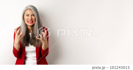 Angry and pissed-off asian senior woman clench fists, grimacing and staring outraged, express hatred and annoyance, standing against white background 101243013