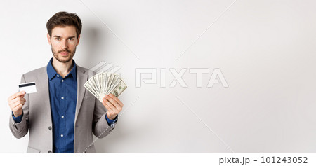 Successful businessman making money, standing in suit with dollar bills and plastic credit card, white background 101243052