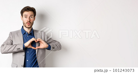 Handsome man looking silly, showing heart love you sign and pucker lips, waiting for kiss from lover, standing in suit on white background 101243073