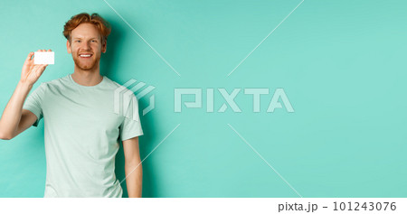 Shopping concept. Handsome redhead man in t-shirt showing plastic credit card and smiling, standing over turquoise background 101243076