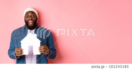 Real estate concept. Happy smiling african-american man holding house model, looking excited at camera, searching for home, standing over pink background Real estate concept. Happy smiling african-american man holding house model, looking excited at camera, searching for home, standing over pink background 101243183