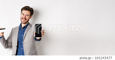 Online shopping. Successful businessman holding plastic credit card and showing mobile screen, smiling satisfied, making money, white background 101243477