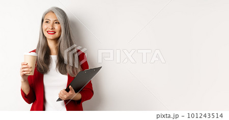Stylish mature businesswoman in red blazer having break, holding clipboard and drinking coffee, looking left with pleased smile, white background Stylish mature businesswoman in red blazer having break, holding clipboard and drinking coffee, looking left with pleased smile, white background 101243514