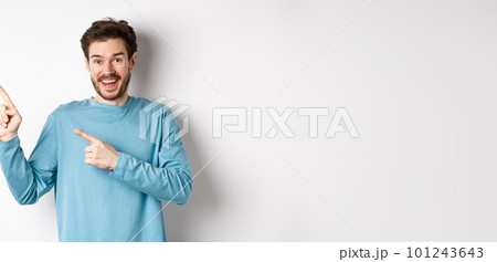 Happy caucasian man in casual blue sweatshirt, pointing fingers at upper left corner, showing link or logo on white background, smiling at camera Happy caucasian man in casual blue sweatshirt, pointing fingers at upper left corner, showing link or logo on white background, smiling at camera 101243643