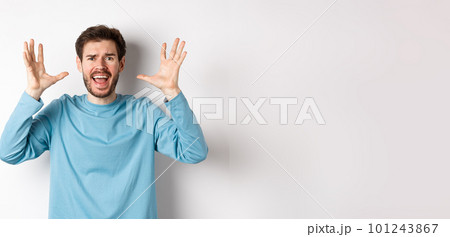 Image of freaked out young man screaming and shaking hands, shouting at camera frustrated or worried, panicking over white background 101243867
