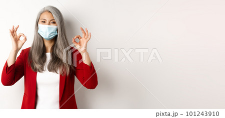 Coronavirus and business concept. Asian female manager in face mask looking cheerful, showing okay signs in approval, white background Coronavirus and business concept. Asian female manager in face mask looking cheerful, showing okay signs in approval, white background 101243910