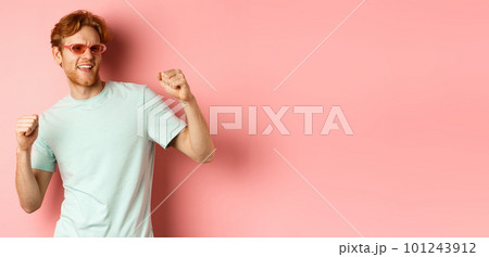 Tourism and vacation concept. Cheerful redhead man having fun at party, dancing and enjoying holiday, standing in sunglasses and t-shirt against pink background Tourism and vacation concept. Cheerful redhead man having fun at party, dancing and enjoying holiday, standing in sunglasses and t-shirt against pink background 101243912