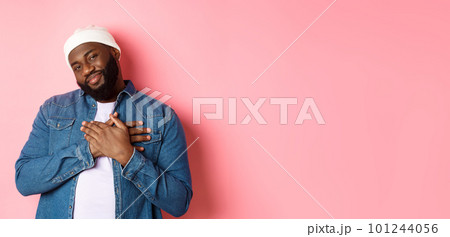 Thankful and touched Black guy saying thank you, smiling adorable and holding hands on heart, appreciate nice gesture, standing over pink background 101244056