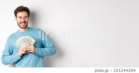 Greedy smiling man showing money and looking right, thinking about shopping, standing over white background 101244269