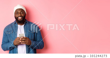 Handsome african-american guy using smartphone, smiling at camera, standing over pink background 101244273