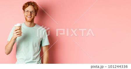 Happy redhead man in glasses and t-shirt drinking coffee and smiling, enjoying lunch break, holding takeaway cup, standing over pink background Happy redhead man in glasses and t-shirt drinking coffee and smiling, enjoying lunch break, holding takeaway cup, standing over pink background 101244336