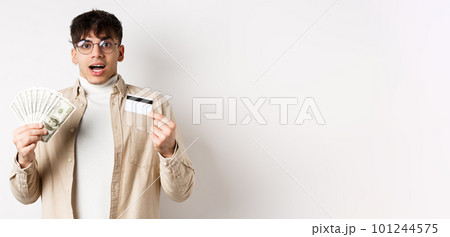 Excited young guy showing dollar bills and credit card, earn money and looking amazed, standing on white background Excited young guy showing dollar bills and credit card, earn money and looking amazed, standing on white background 101244575