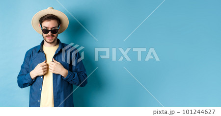 Handsome young man going on vacation, adjusting shirt, wearing sunglasses and straw hat. Concept of summer holiday Handsome young man going on vacation, adjusting shirt, wearing sunglasses and straw hat. Concept of summer holiday 101244627