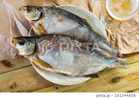 Dried bream lies on plate with imitation of antiquity. Fish complemented by glass of beer Dried bream lies on plate with imitation of antiquity. Fish complemented by glass of beer 101244838