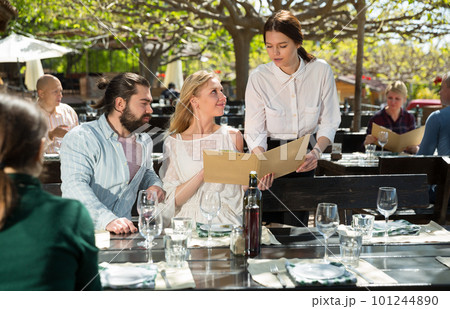 Waitress helping visitors with menu on outdoor terrace 101244890