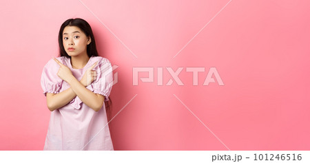 Clueless cute asian girl pointing sideways and look confused, cant make decision, standing hesitant against pink background 101246516