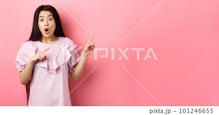 Excited asian woman look amazed, pointing right and gasping fascinated, checking out advertisement, standing on pink background 101246655