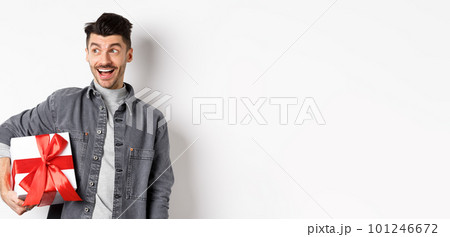 Cheerful handsome guy looking at empty space with amazed smile, checking out special valentines day offer, holding big romantic gift box, standing on white background Cheerful handsome guy looking at empty space with amazed smile, checking out special valentines day offer, holding big romantic gift box, standing on white background 101246672