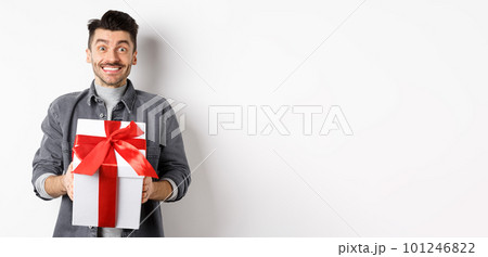 Cheerful caucasian guy holding surprise gift, receive present on holiday and smiling thankful, looking grateful at camera, celebrating Valentines day, white background 101246822