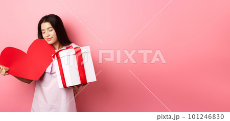 Valentines day concept. Romantic asian teen girl receive gifts on white day from lover, hugging big red heart card and present in box, smiling sensual, pink background Valentines day concept. Romantic asian teen girl receive gifts on white day from lover, hugging big red heart card and present in box, smiling sensual, pink background 101246830