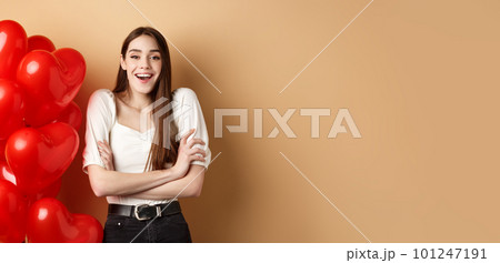 Valentines day concept. Beautiful young woman having fun, laughing and smiling at camera, standing near romantic heart balloons, beige background Valentines day concept. Beautiful young woman having fun, laughing and smiling at camera, standing near romantic heart balloons, beige background 101247191