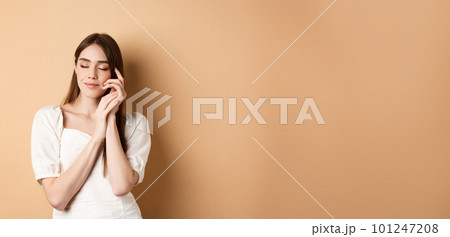 Tender and romantic woman close eyes, gently touching soft smooth skin, smiling dreamy while standing against beige background 101247208