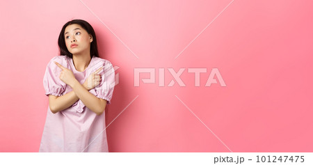Indecisive asian woman cant decide, pointing fingers sideways and look pensive aside, making choice, standing confused on pink background Indecisive asian woman cant decide, pointing fingers sideways and look pensive aside, making choice, standing confused on pink background 101247475