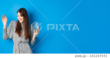 Celebration and party concept. Dancing girl holding glass of champagne, having fun at holiday, celebrating birthday, standing on blue background 101247541