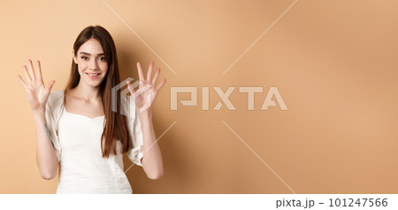 Attractive young woman show fingers number ten, smiling and looking confident, standing on beige background 101247566