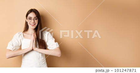 Smiling girl in glasses say thank you, show namaste gesture, express gratitude, standing pleased on beige background 101247871